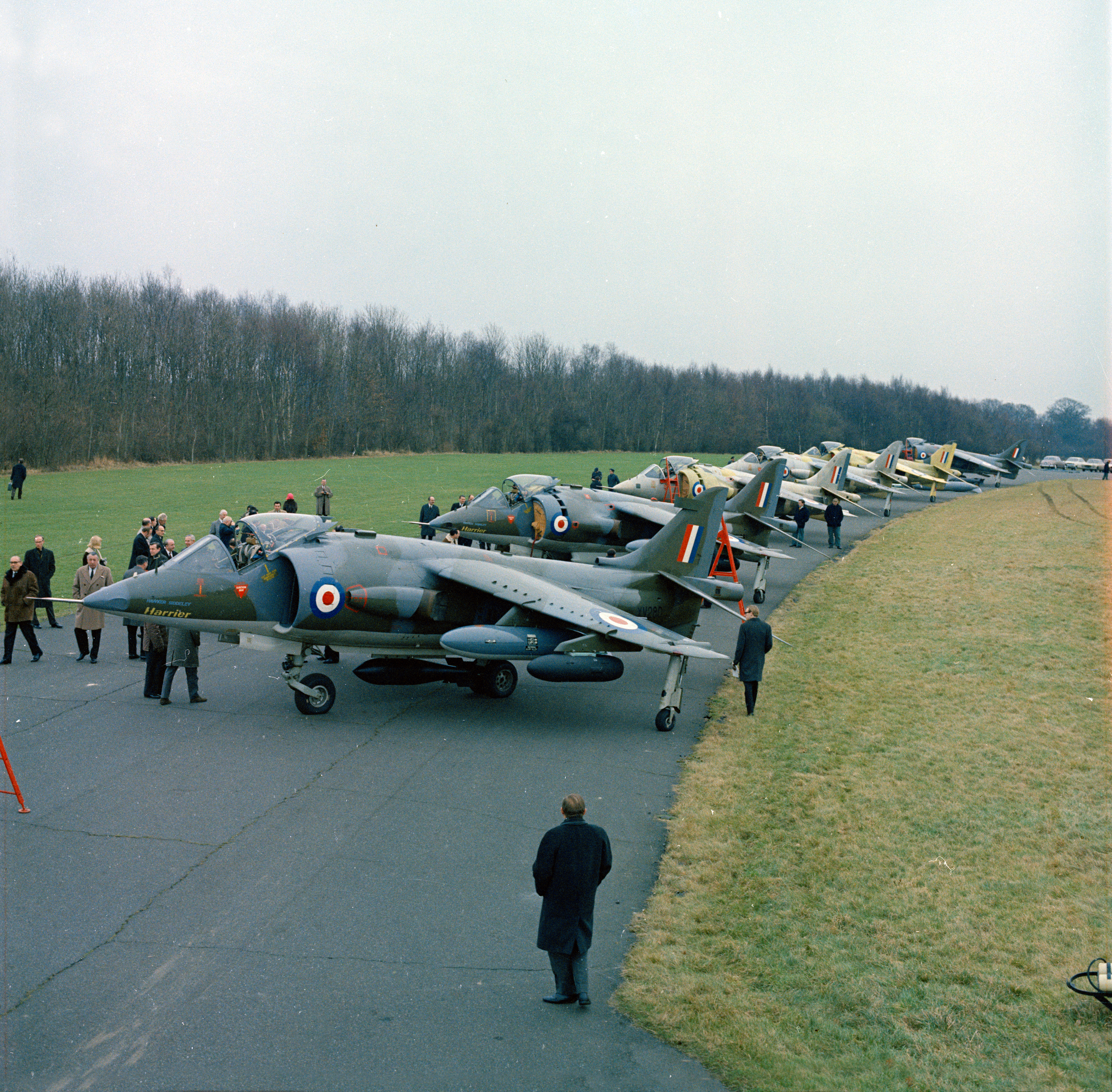 Sur la photo, six Hawker Siddeley Harrier GR.1 de pré-production photographiés dans les installations d'essais du fabricant à l'aérodrome de Dunsfold, dans le Surrey, en 1968. Le premier escadron de la RAF à être équipé du Harrier GR.1, du 1er Escadron, a commencé à se convertir à l'avion à RAF Wittering en avril 1969. Pendant le service du Harrier, la RAF a positionné la majeure partie des avions en Allemagne de l'Ouest pour se défendre contre une éventuelle invasion de l'Europe occidentale par les forces du Pacte de Varsovie ; les capacités uniques du Harrier ont permis à la RAF de disperser ses forces loin des bases aériennes vulnérables. *Certaines de ces images ont été esquivées et brûlées et ont été retouchées pour éliminer uniquement les détritus, la poussière et les rayures*