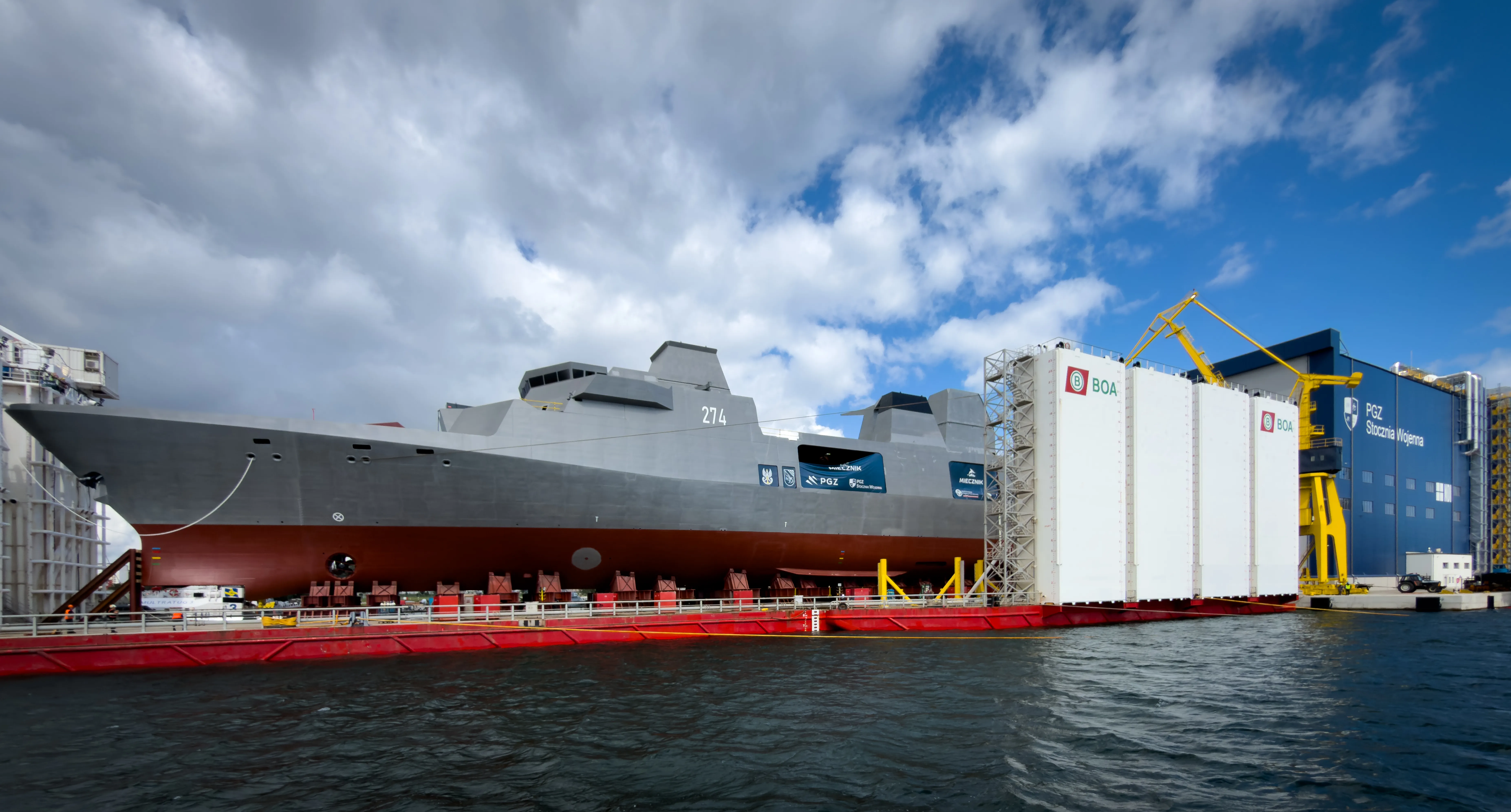 Une vue large montre la future frégate polyvalente de la Marine polonaise ORP Wicher, fanion numéro 274, à bord de la barge semi-submersible de transport lourd BOABARGE 33 avec le hall de coque PGZ Stocznia Wojenna visible derrière elle à Gdynia, en Pologne, le 11 août 2026. La frégate a été assemblée et intégrée à l'intérieur du hall avant d'être déployée et positionnée sur la barge pour son baptême et son lancement. (Photo de Mateusz Wlodarczyk/NurPhoto via Getty Images)
