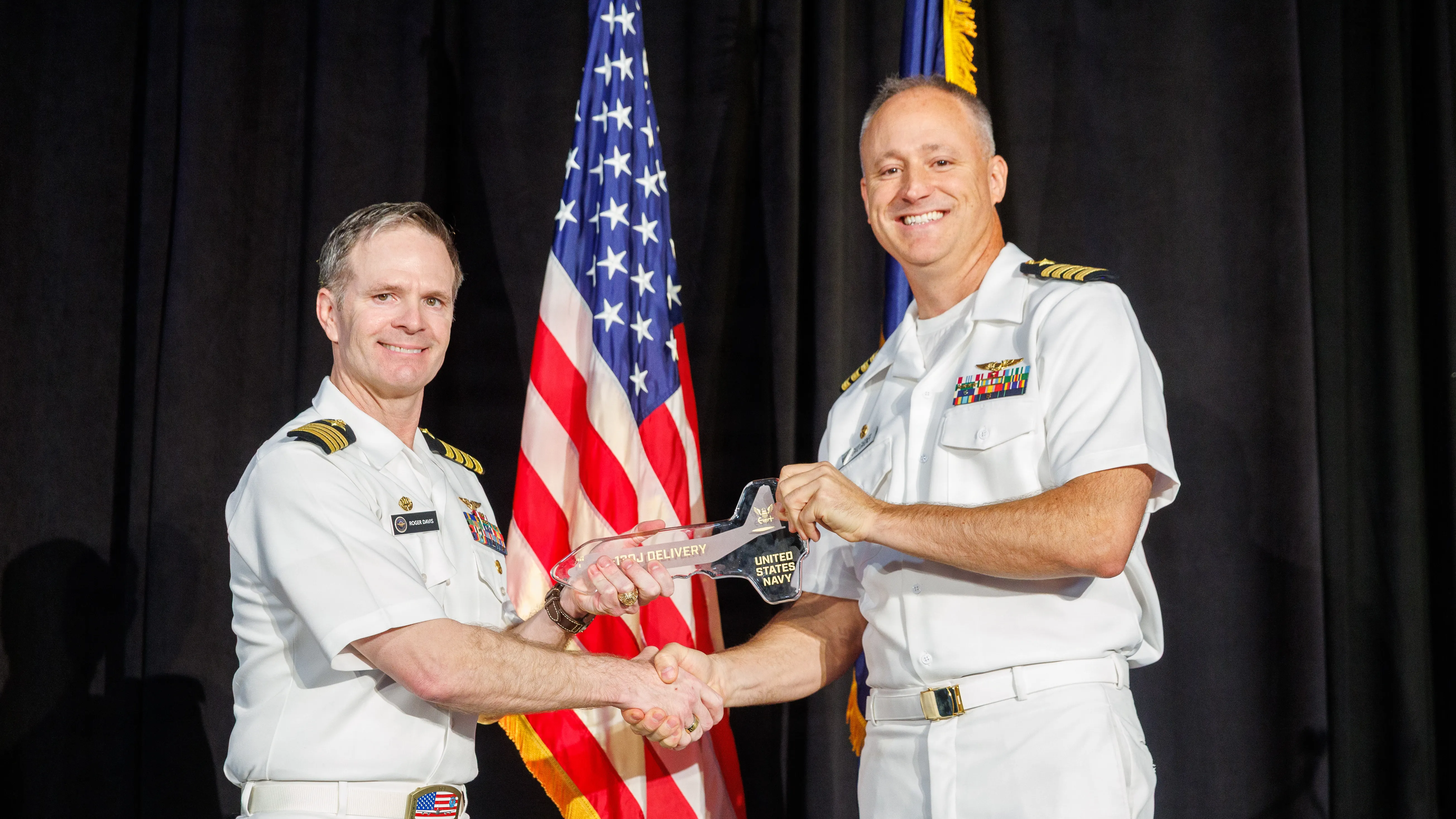 Le capitaine Roger Davis, à gauche, responsable du programme de commandement, de contrôle et de communications stratégiques aéroportés (PMA-271), présente une clé de cérémonie au capitaine David Gardner, commodore de l'aile des communications stratégiques 1 (SCW 1), lors de la cérémonie de livraison du C-130J-30 le 15 octobre 2026 à Marietta, en Géorgie. Cette remise symbolique marque la transition de la nouvelle cellule vers la prochaine phase de modification du système de mission, d'essais au sol et d'essais en vol de développement, jetant ainsi les bases de la mise en service du futur E-130J « Phoenix II ». (Photo fournie par Lockheed Martin par Thinh D. Nguyen)